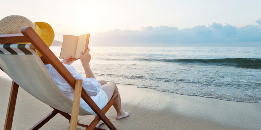 Vrouw in een ligstoel op het strand met een boek in haar handen, ter illustratie van het thema zomerse boekentips